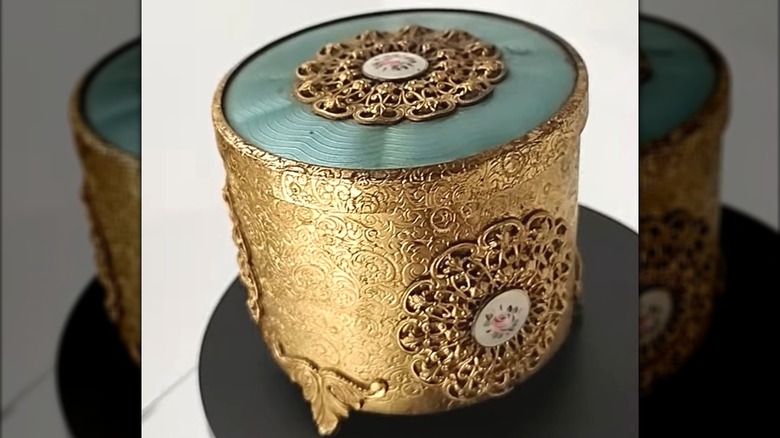An antique Thorens gold-tone filigree and guilloche music box with a mirrored powder puff holder