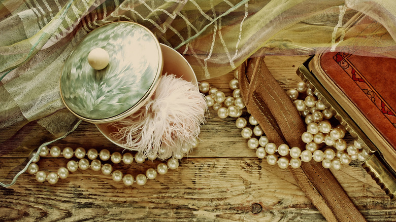 A collection of vintage accessories, powder box, scarf, necklace and handbag on wooden table