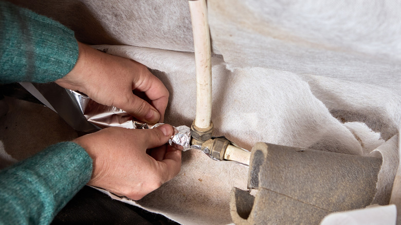 Hand wrapping water heater pipe in insulating foil