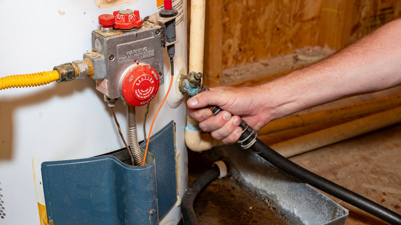 Person's hand connecting drain hose to a water heater