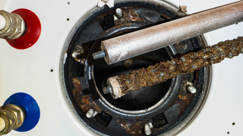 Two different anode rods 9one rusted, another brand new) with a water heater in the background