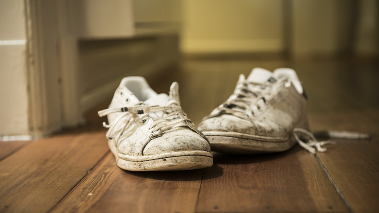 A pair of white dirty lace-up shoes on a wooden floor