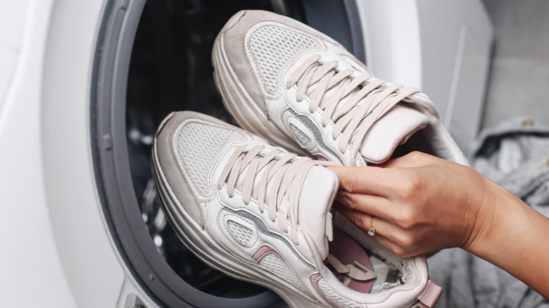 A woman putting a pair of white shoes into a washing machine