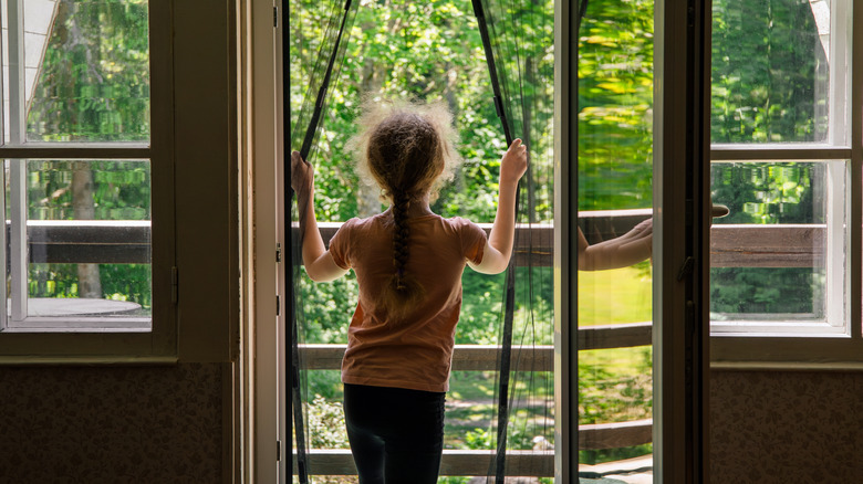 Child opening a magnetic fly curtain in doorway to outdoor porch and yard
