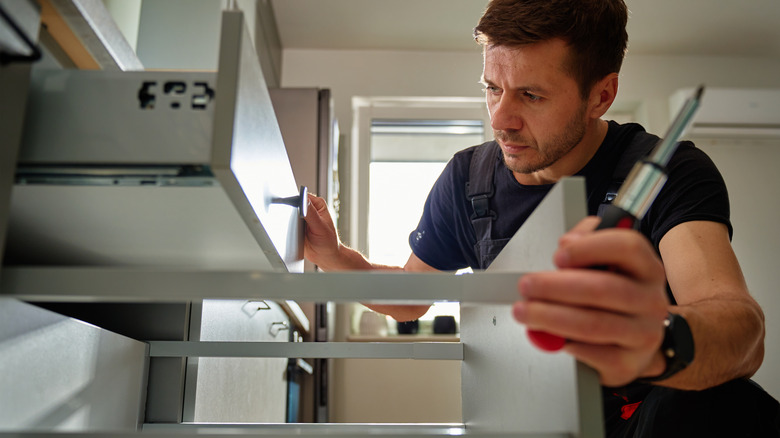 man holding screwdriver while adjusting metal and wooden drawers