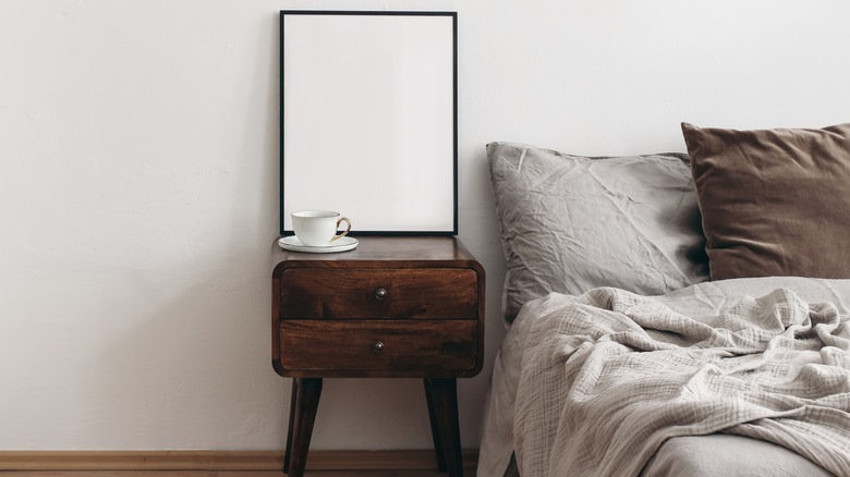 Dark wooden nightstand with tea cup beside gray bed