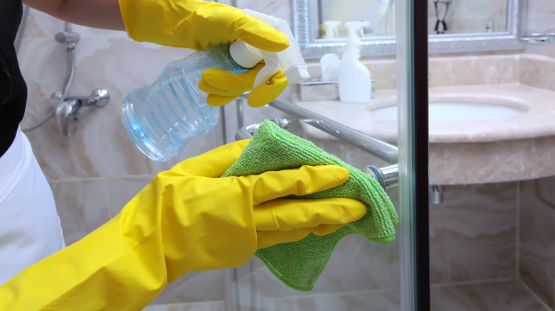 Hands with rubber gloves using a soft cloth to clean a shower door