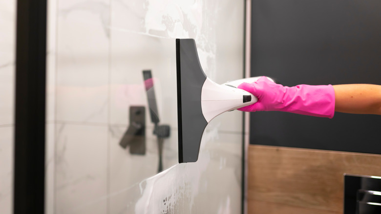 Close-up of pink-gloved hands squeegeeing a shower door