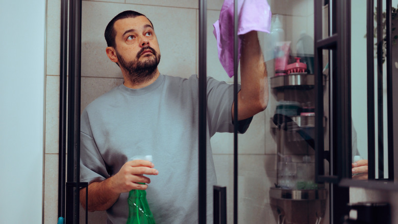 Close-up of a man cleaning his shower door with a green bottle in one hand