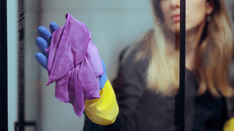 A woman wiping a shower door with a purple cloth