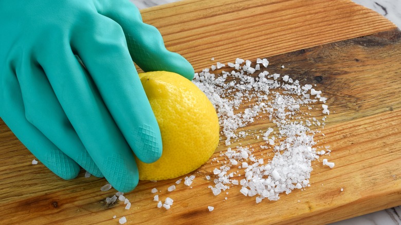 A gloved hand is rubbing a lemon half, cut side down, into a pile of salt