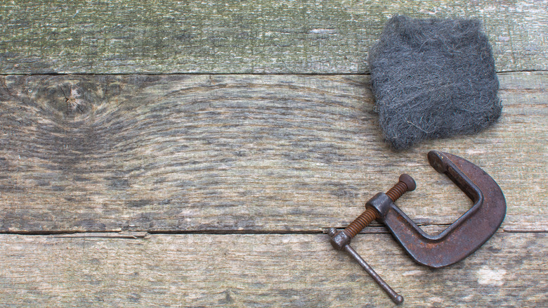 A steel wool pad lies next to a rusted clamp on a work bench