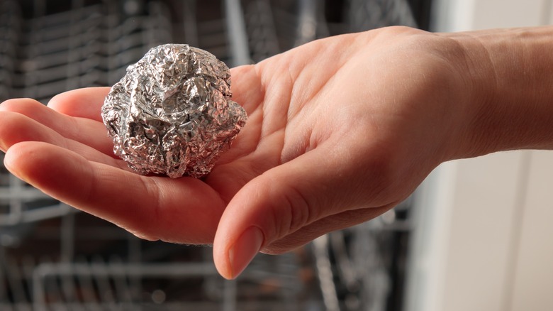 A hand is holding a crumpled ball of aluminum foil, about the size of a tennis ball