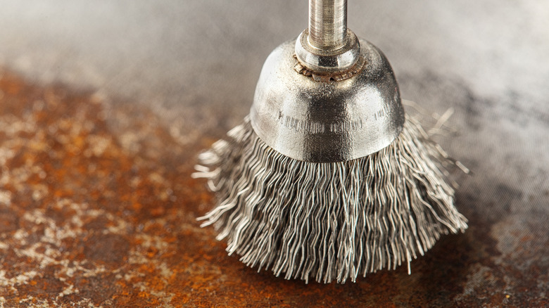 A drill's wire brush attachment is seen cleaning up a flat, rusted surface