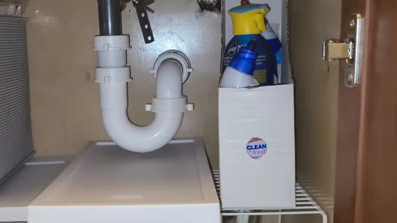 White paper file holder holding cleaning supplies underneath a cabinet