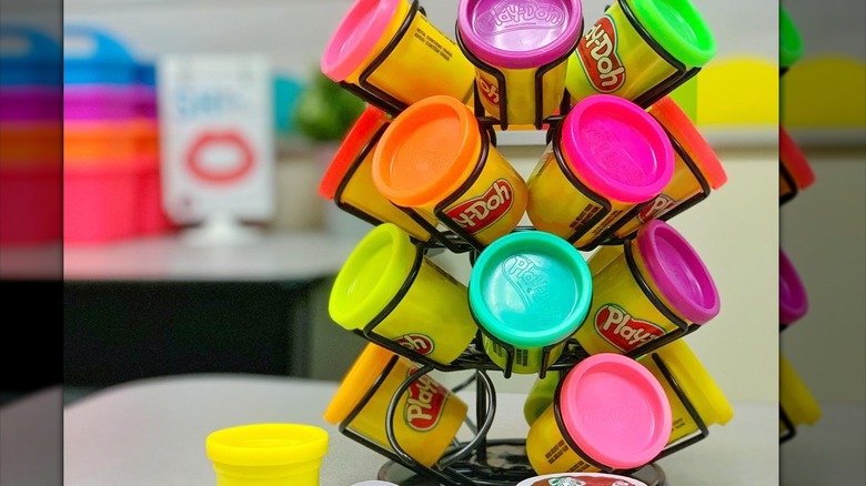 Small canisters of Play-Doh stored inside of a coffee organizer, two coffee capsules in front of it on a table