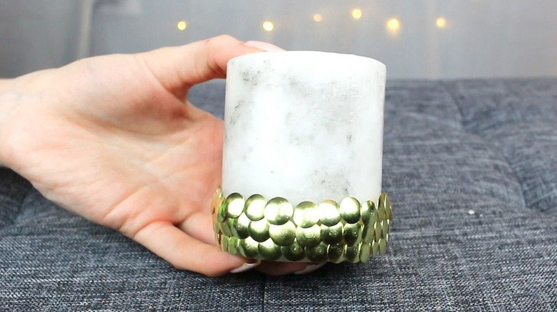 White pillar candle decorated with gold thumbtacks around the base.