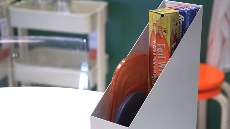 White metal magazine holder storing boxes of foil and wrap.