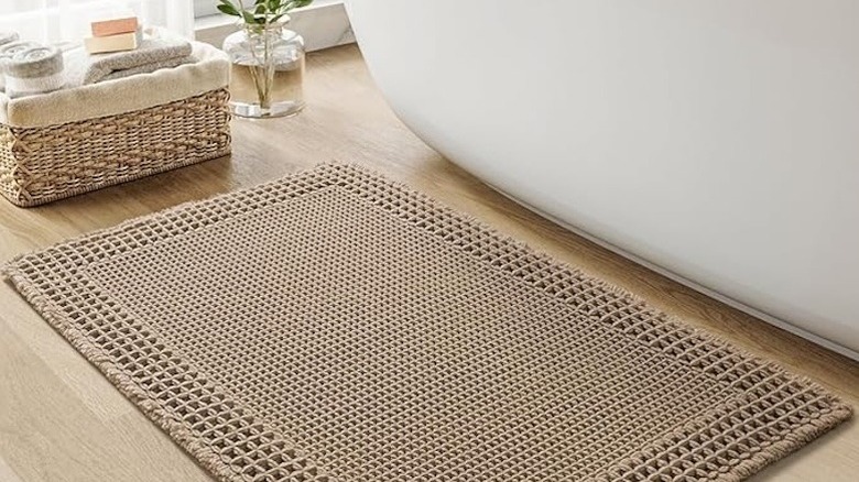 A tan woven bath mat on a wood floor.