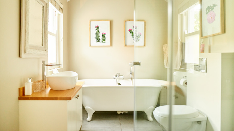A bright bathroom with a vintage tub and wall art.