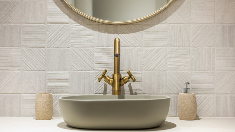 A beige tile backsplash and a brushed gold sink