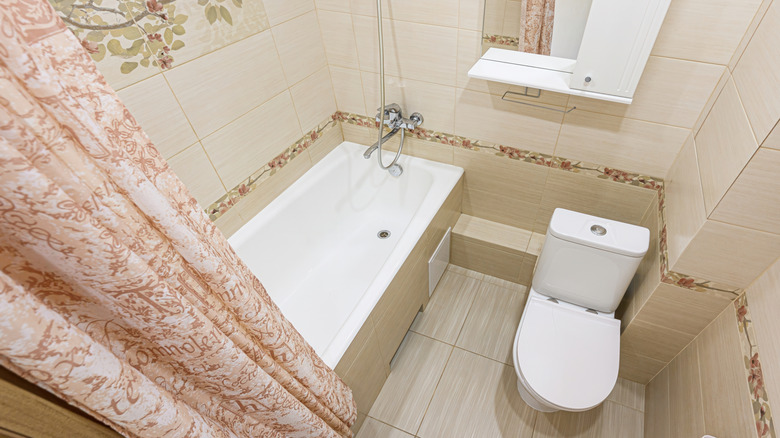 A small beige bathroom with a vintage curtain.