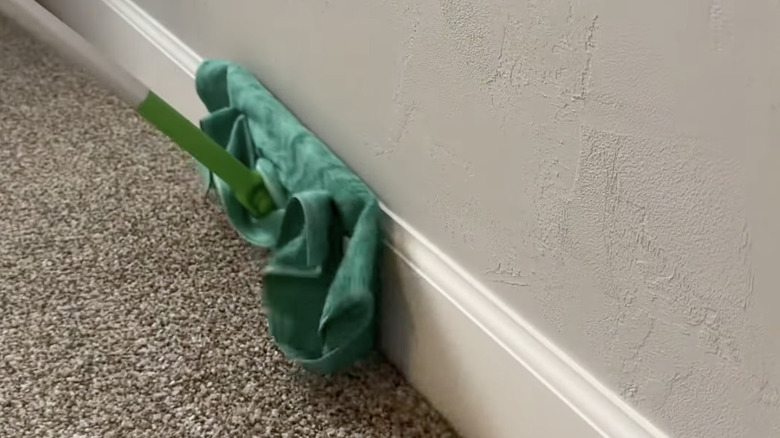 A mop wrapped in a microfiber cloth cleaning a baseboard.