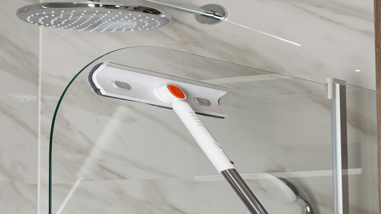 Using a mop to clean the glass walls of a shower stall.