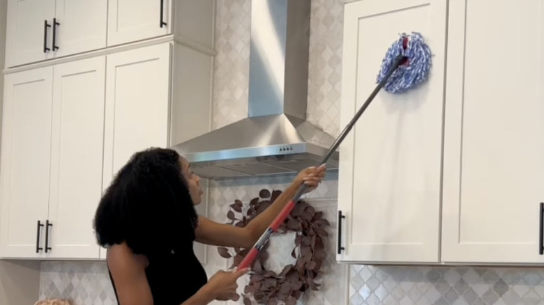 A woman mops her kitchen cabinets.