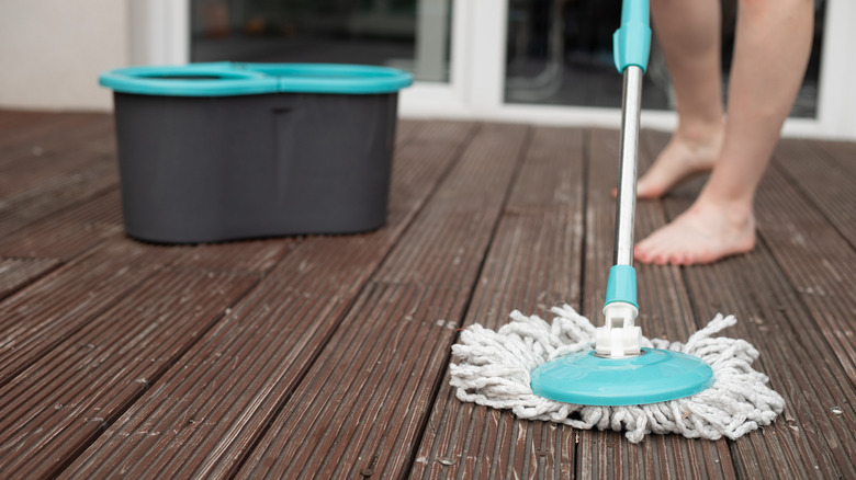 A homeowner washes a wooden deck with a mop.