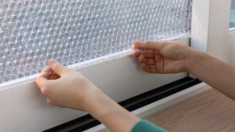 Hands applying bubble wrap to a window
