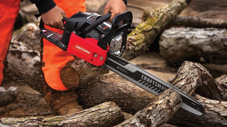 Person using the Craftsman S205 chainsaw to cut a pile of wooden logs
