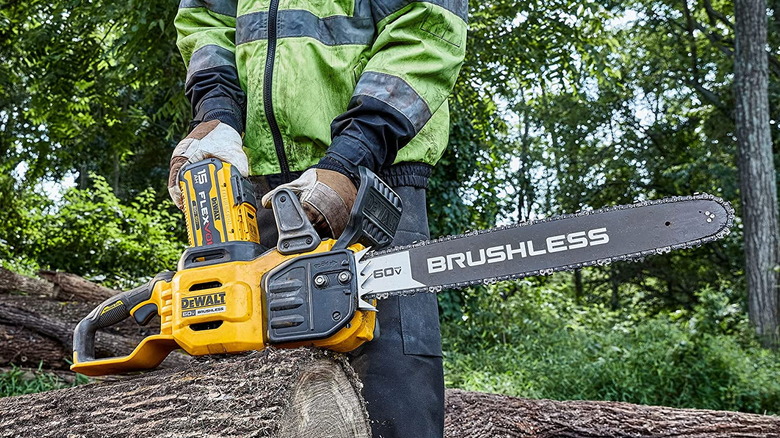 Person resting the DeWalt DCCS677B on top of a cut log with trees in the background