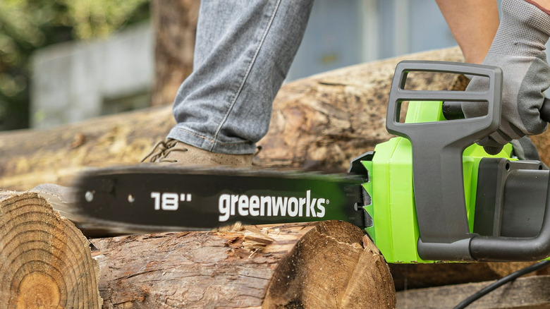 Person using the Greenworks 18-in Corded Electric Chainsaw to cut a wooden log