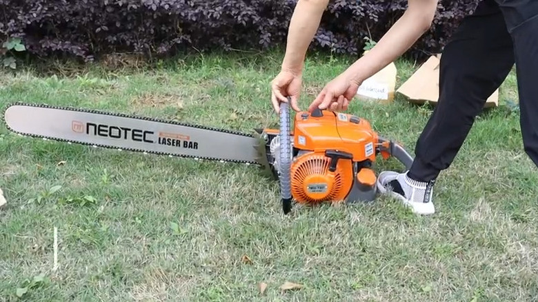 Person starting the NEO-TEC 36-inch gas chainsaw on the grass outside