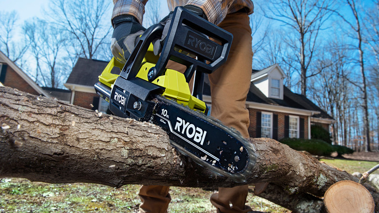 Person using the Ryobi 40V 10 in. Chainsaw to cut a log outside in front of a house