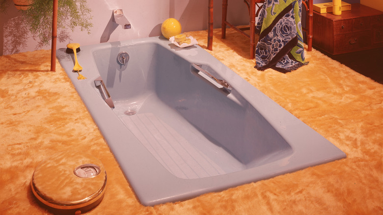 A retro bathroom with sunken powder blue tub surrounded by orange carpet.