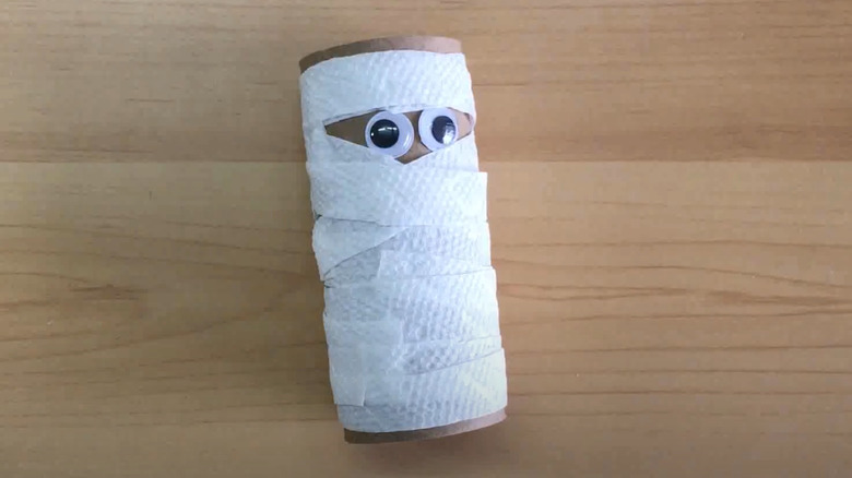 Toilet paper mummy with googly eyes on wood table