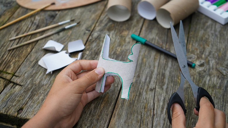 A hand with scissors crafting with toilet paper rolls
