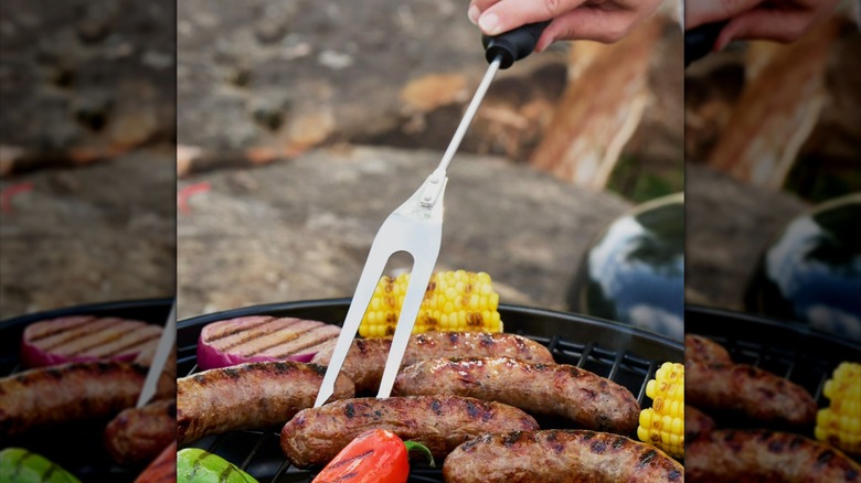 Meat grilling fork stabbing a sausage on the grill