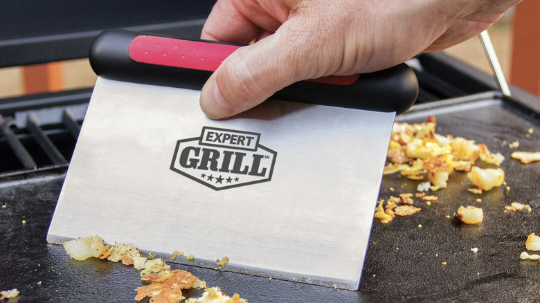 Metal griddle scraper pushing food on a griddle grill