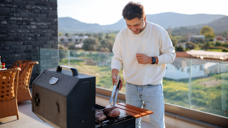 Young man using grilling tongs to turn meat on grill