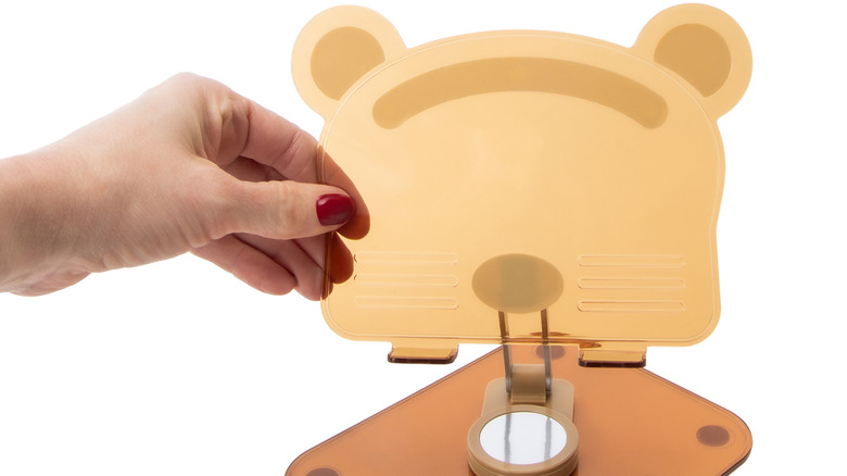 A hand with red nails holding a bear-shaped tablet stand