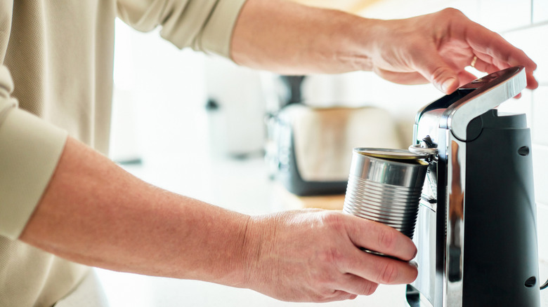 A man uses an electric can opener to open a can