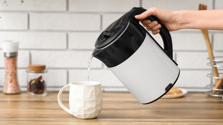 Woman pours hot water from an electric kettle