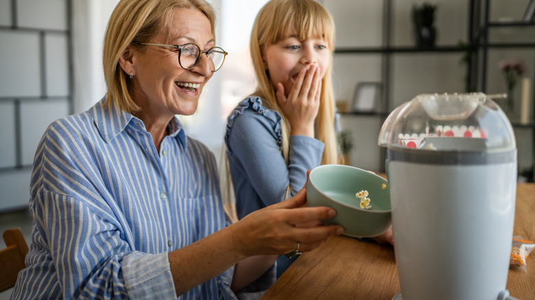 Child and grandmother make popcorn in a popcorn maker