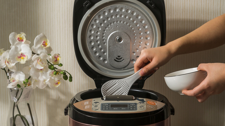Person scooping rice from a rice cooker into a bowl