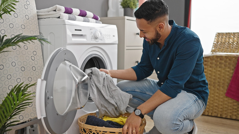 Young man placing clothes into the washer in laundry room