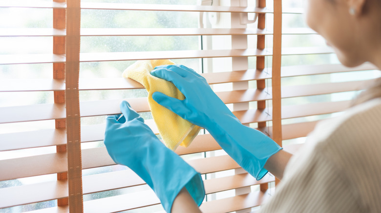 Woman dusting the blinds using a microfiber cloth