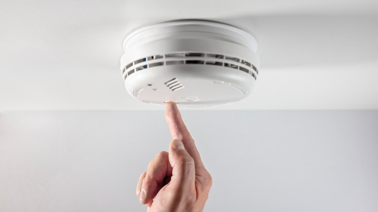 Finger pushing smoke detector button, testing or replacing battery